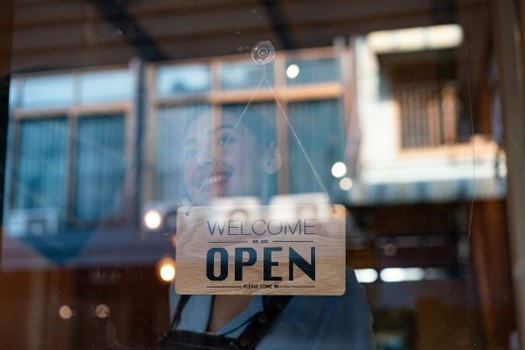 small business woman looking out window with open sign